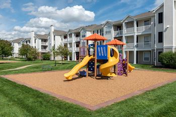 A playground with a yellow slide and a purple slide in front of apartment buildings.